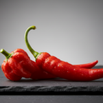 Frische rote Chilischoten auf dunkler Steinplatte.