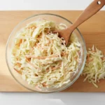 Gläserne Schüssel Krautsalat mit Karotten auf Holzbrett.
