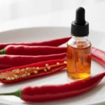 Rote Chilischoten und Ölfläschchen mit Tropfer auf Teller