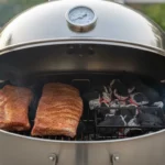 Kugelgrill mit zwei großen Fleischstücken und Holzkohle.