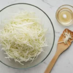 Gehobelter Weißkohl in Glasschüssel, Holzlöffel daneben.